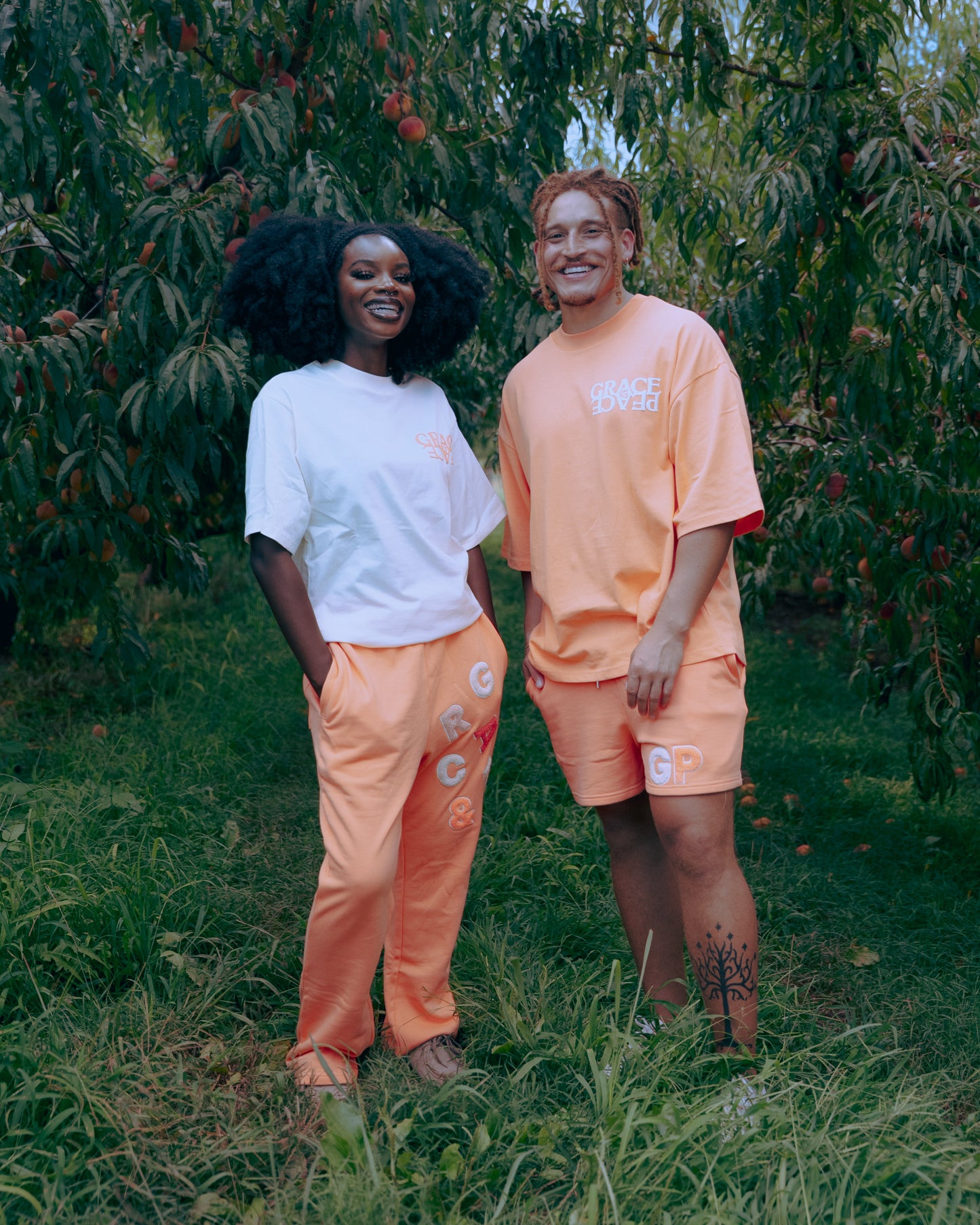 Two people standing in an orchard wearing matching outfits.