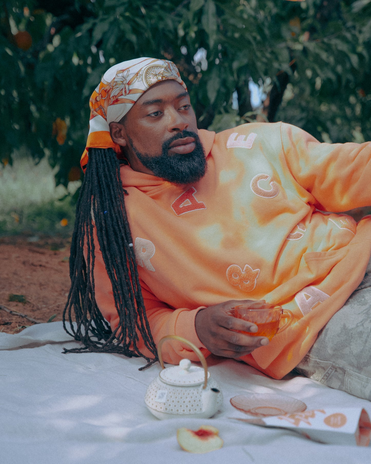 Man in an peach hoodie sitting on a blanket outdoors, Drinking tea