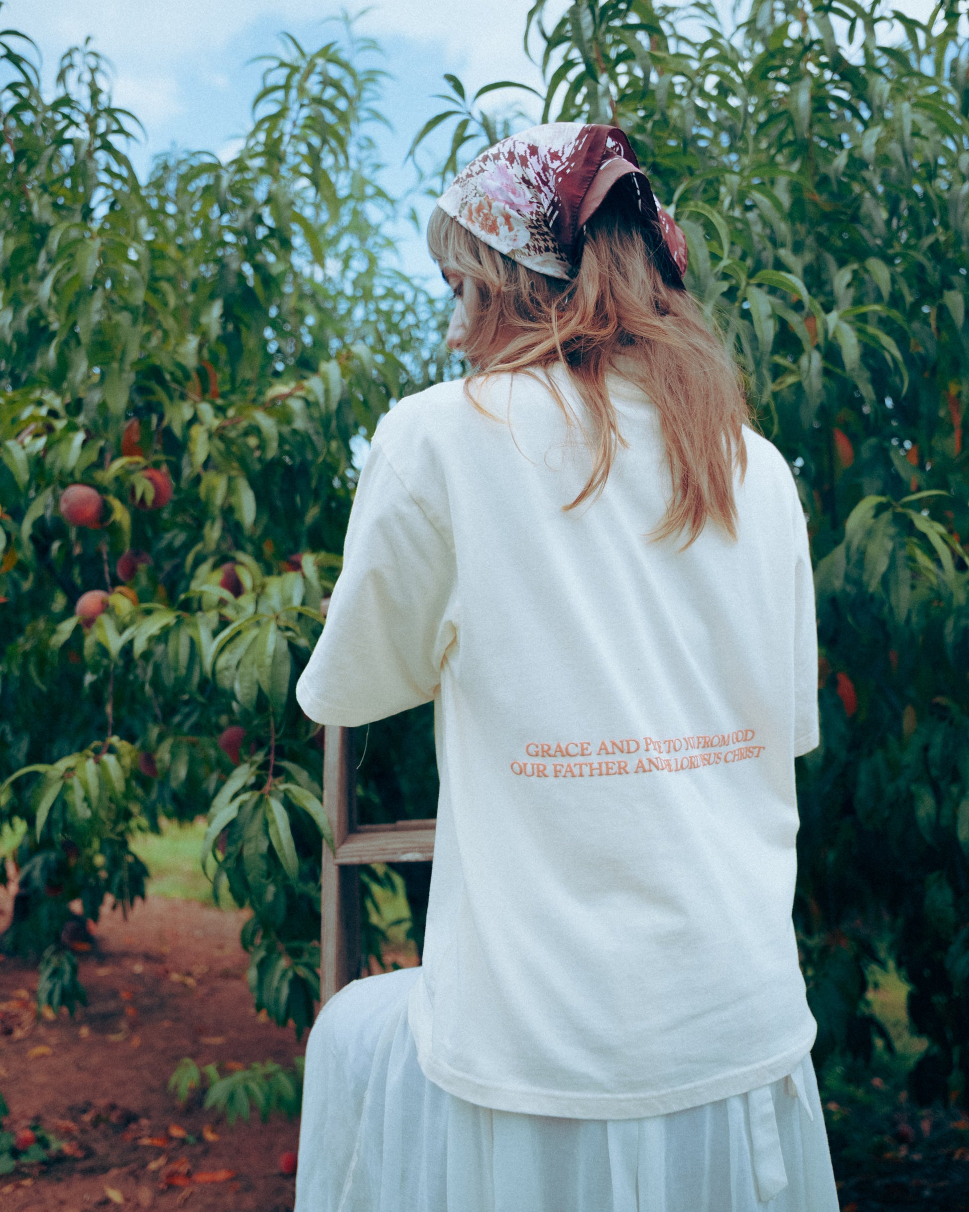 Person wearing a cream shirt with peach text in an orchard