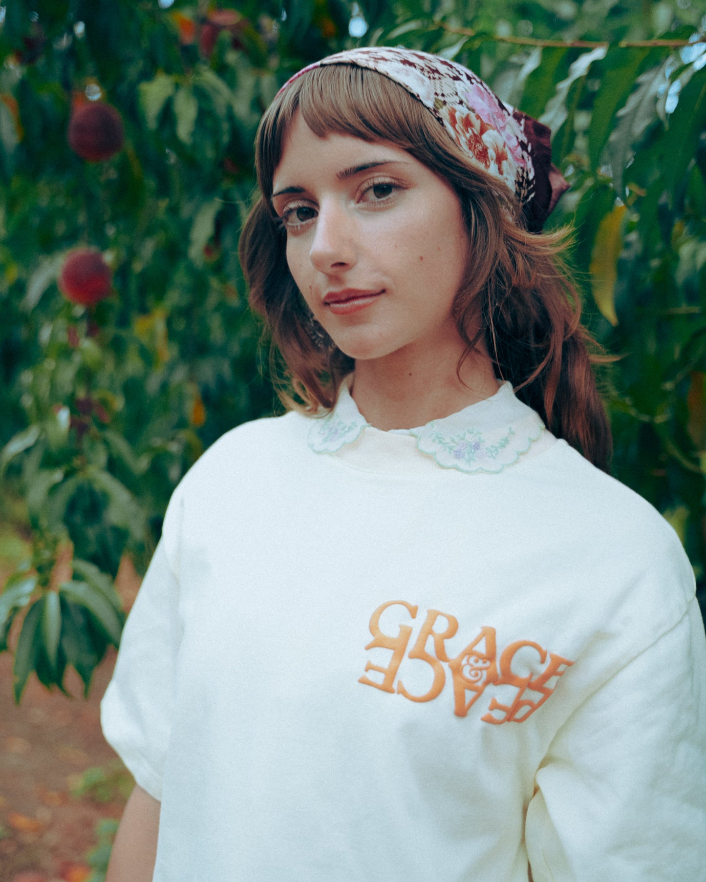 Person wearing a cream shirt with peach text in an orchard
