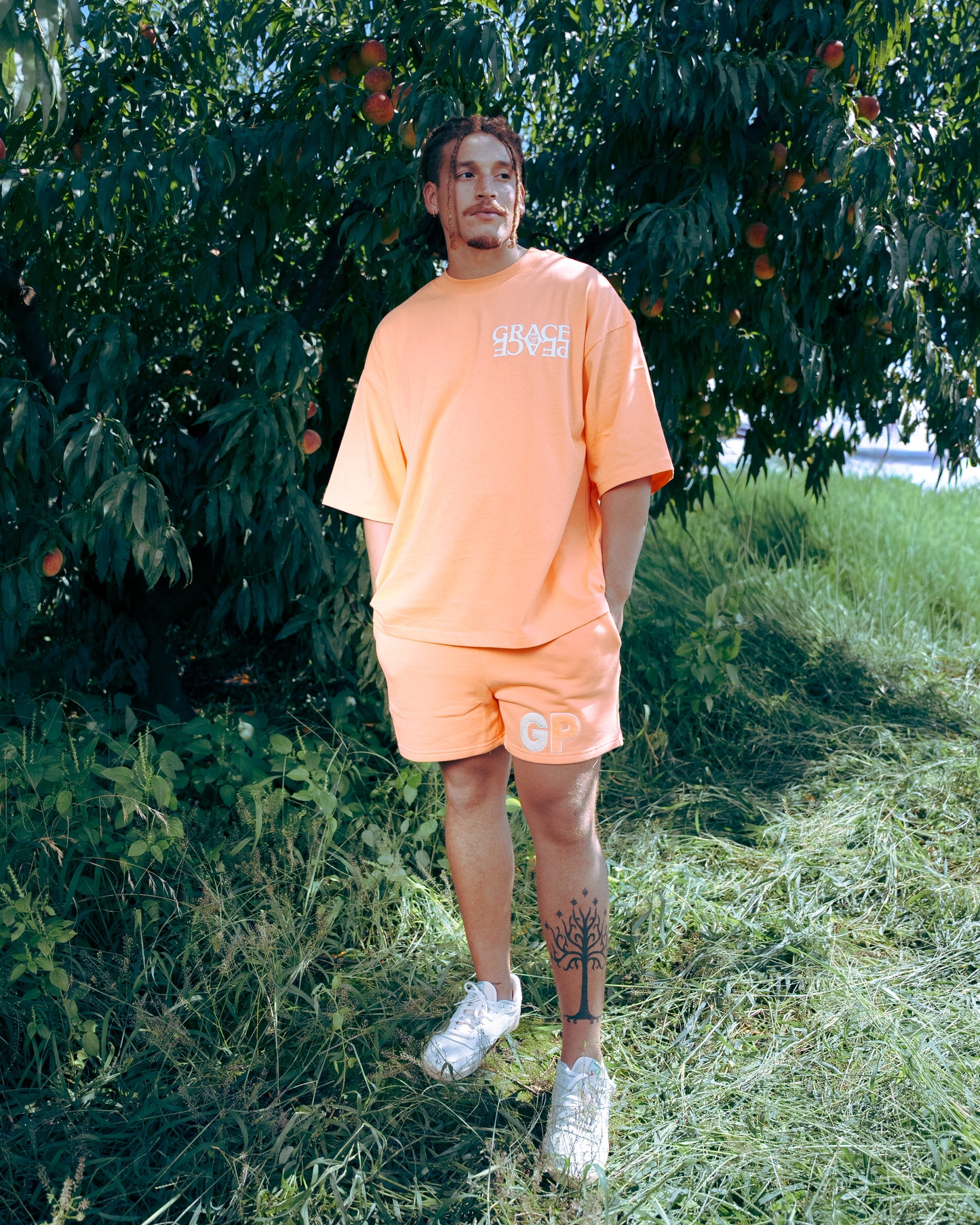 Man wearing an peach  t-shirt and shorts standing in a peach orachard 
