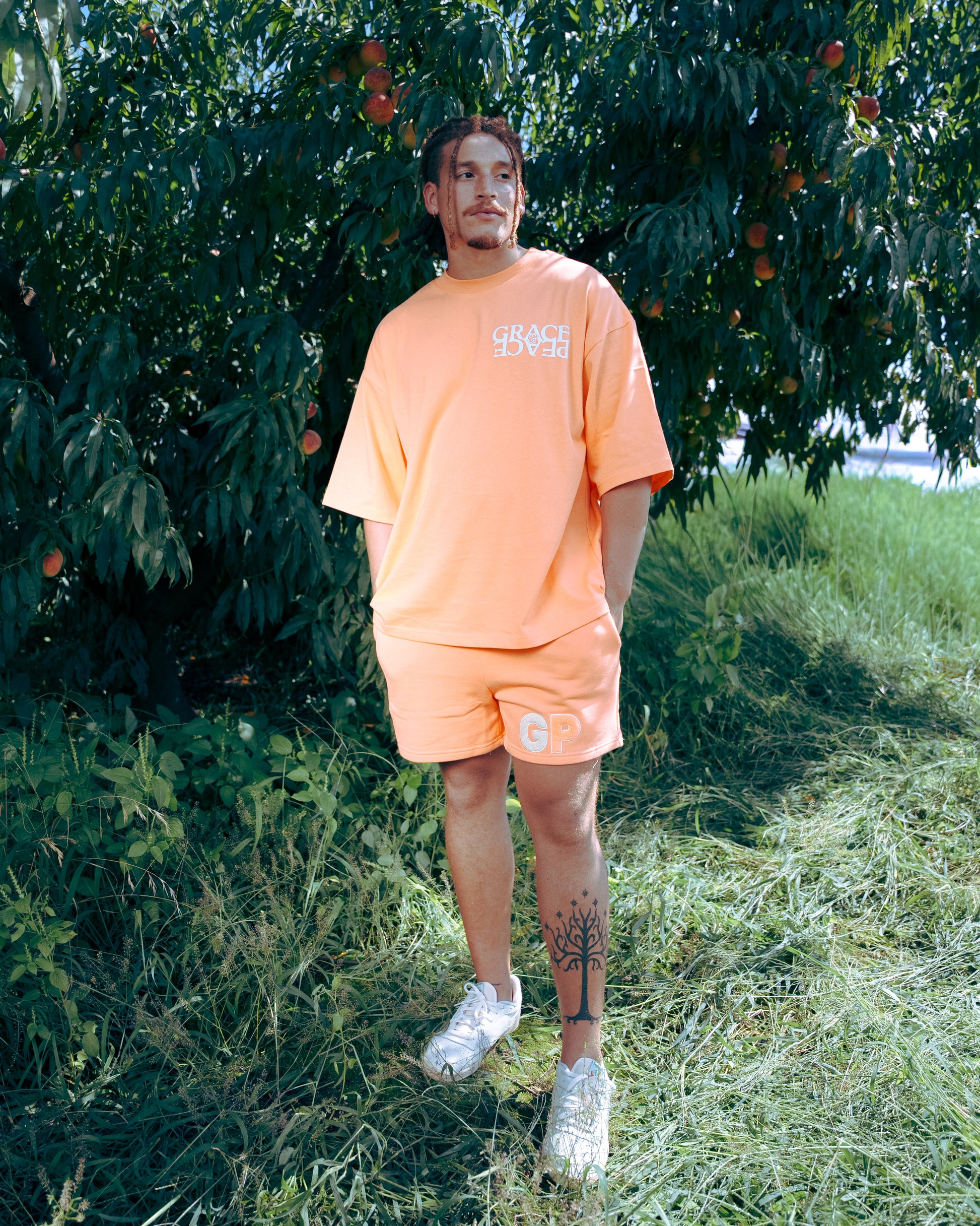 Man wearing an peach  t-shirt and shorts standing in a peach orachard 