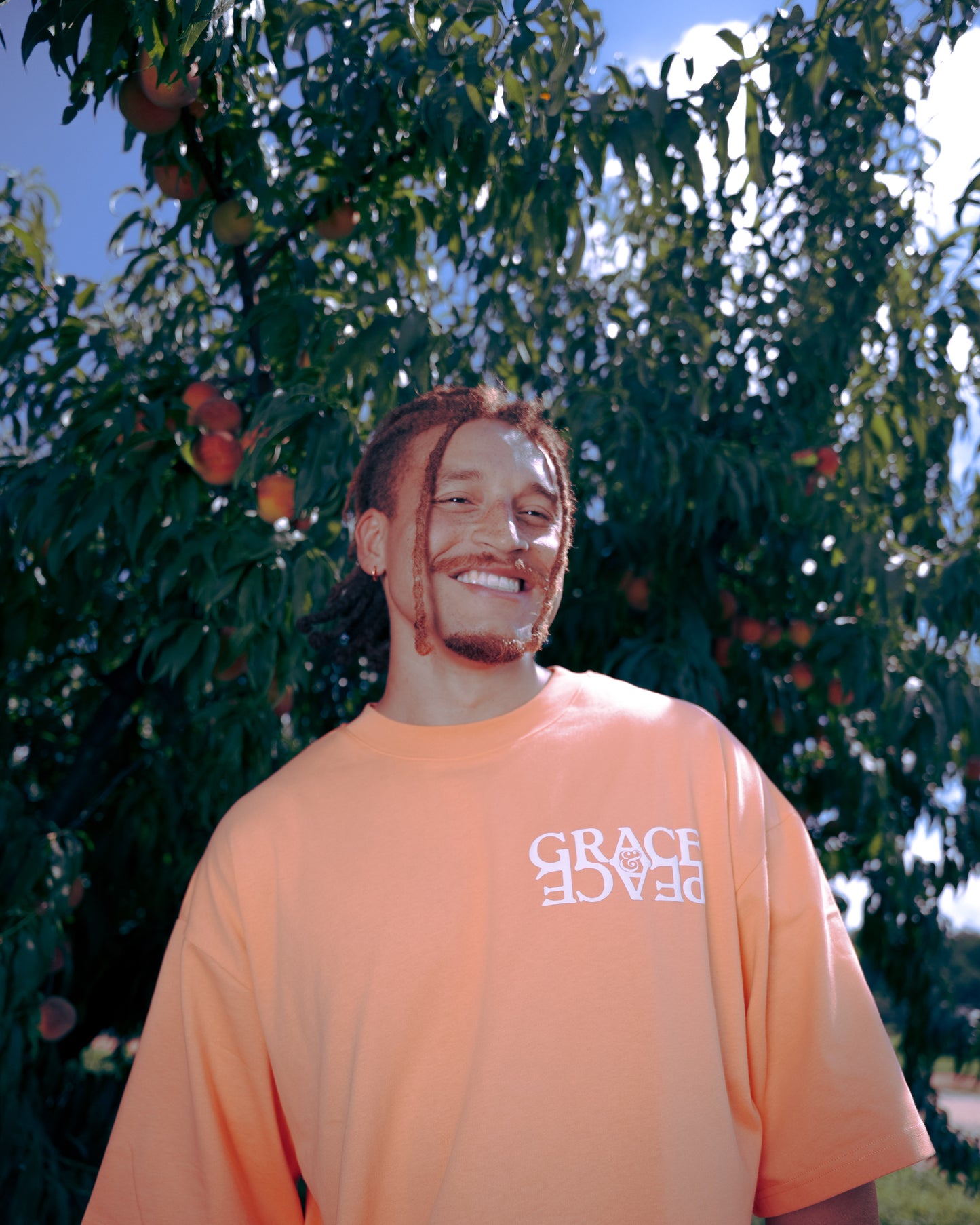 Person wearing a peach-colored t-shirt with text, standing in front of a peach tree