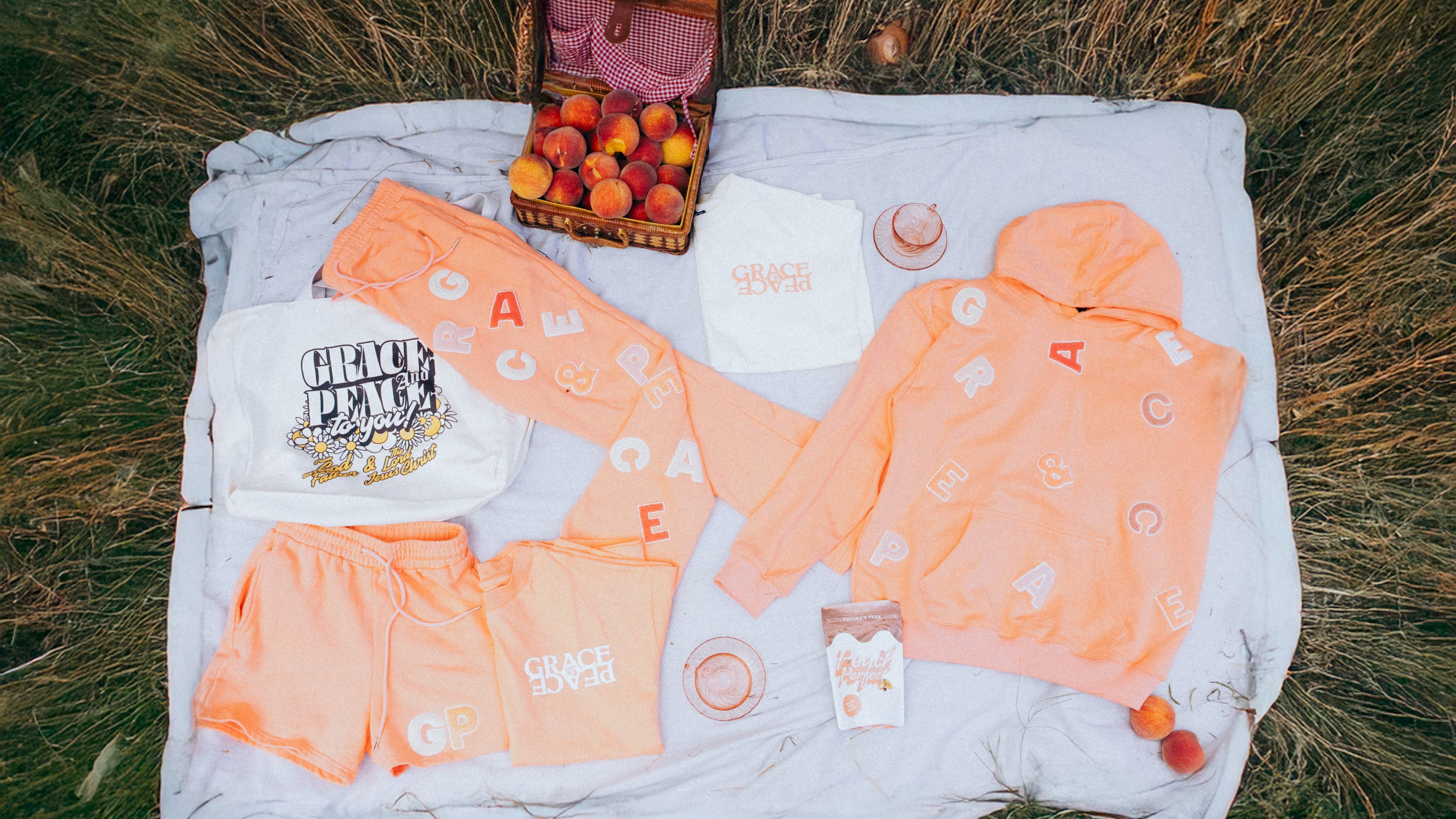 Collection of peach-colored clothing and accessories on a blanket in a grassy field.